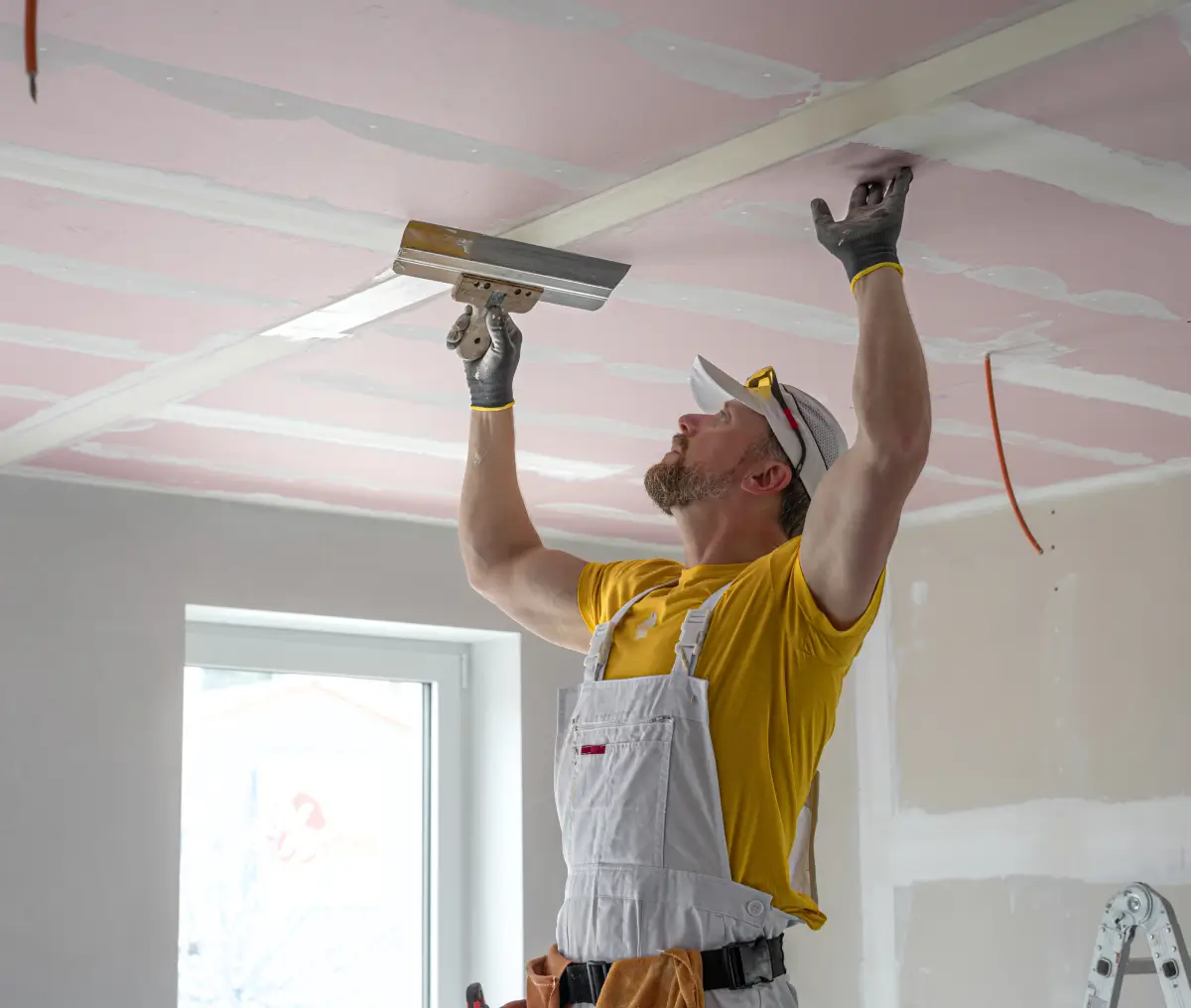 Worker plastering ceiling in a room.