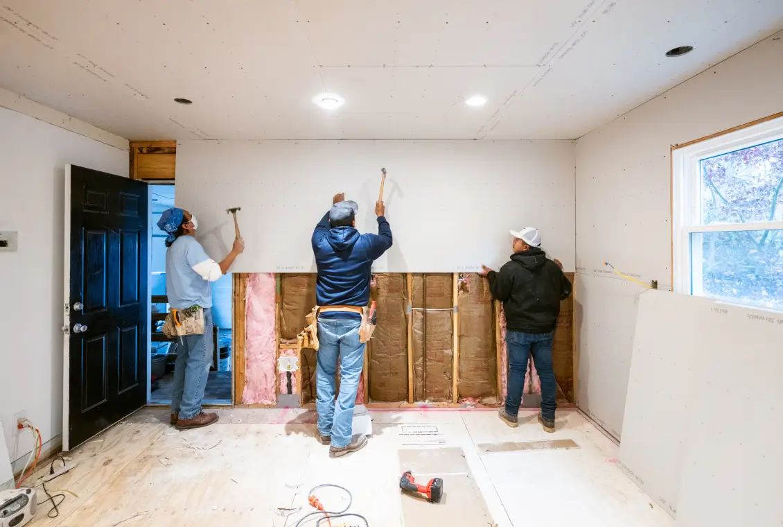 Workers installing drywall in a room.