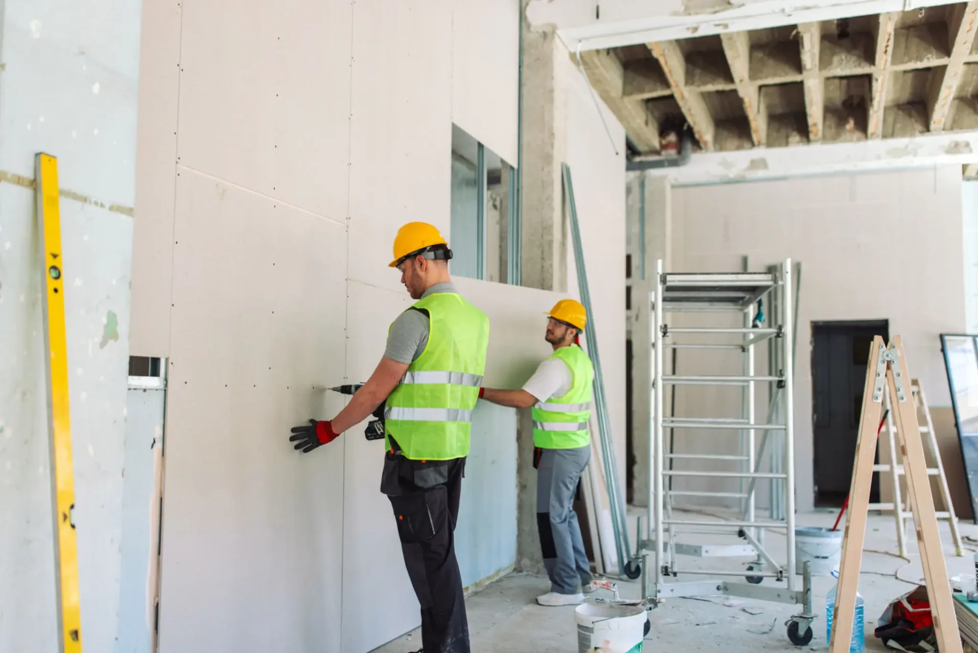Two construction workers installing drywall in a building under construction.